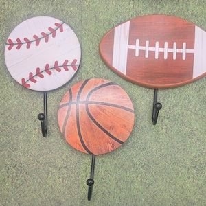 May include: Three decorative wall hooks shaped like a baseball, basketball, and football. Each hook is made of wood and painted to resemble the sport.
