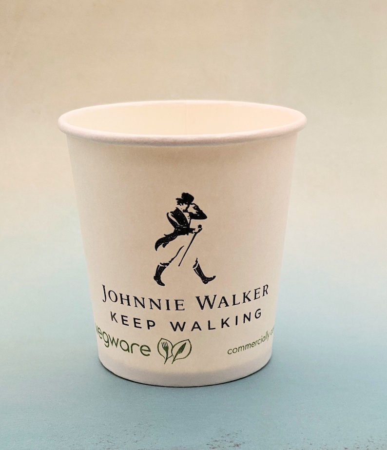 May include: White paper cup with a black and white logo of a man walking with a cane. The logo says "Johnnie Walker Keep Walking". The cup also has the words "egware" and "commercially" printed on it.