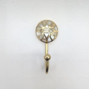 May include: A decorative gold-colored wall hook with a round, inlaid mother-of-pearl design. The hook has a simple, elegant design, perfect for hanging lightweight items. The hook is approximately 4 inches long.