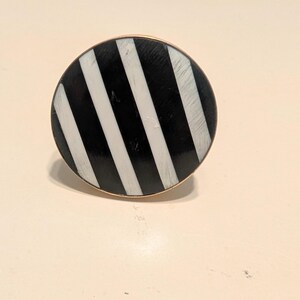 May include: A round cabinet knob with a black and white striped design. The knob has a gold-colored base and is set against a neutral background. This decorative hardware is suitable for drawers and cabinets.