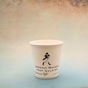 May include: A white paper cup with a black and white logo that says "Johnnie Walker Keep Walking" and a green leaf design. The cup is on a light blue background.