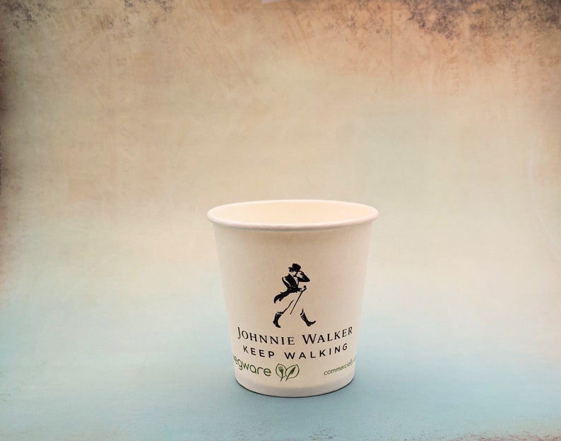 May include: A white paper cup with a black and white logo that says "Johnnie Walker Keep Walking" and a green leaf design. The cup is on a light blue background.
