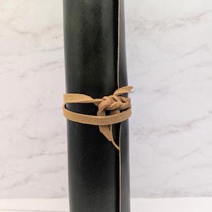May include: A dark green leather journal with a brown leather strap tied around it.