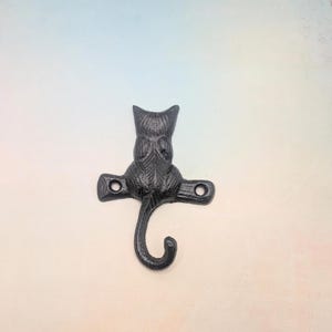 May include: Black cast iron cat hook with a curled tail. The hook is designed to look like a cat sitting with its back to the viewer.