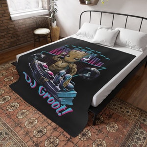 May include: A black fleece throw blanket with a retro-style graphic of a green alien character wearing headphones and holding a DJ mixer. The text "DJ Groot!" is printed in pink and blue on the blanket.