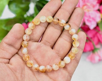 May include: A bracelet made of small, round, light yellow and white beads. The beads have a sparkly, iridescent quality.