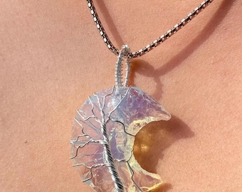 May include: A silver chain necklace with a crescent moon pendant made of clear iridescent glass. A silver wire tree is wrapped around the glass moon.