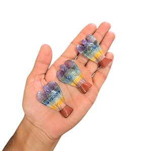 Op de afbeelding: Drie kleine engelbeeldjes gesneden uit veelkleurig steen. De engelen zijn gelaagd met zeven chakrakleuren, waaronder paars, blauw, groen, geel, oranje en rood.