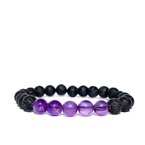 Puede incluir: Un brazalete de cuentas de lava negra y amatista. El brazalete tiene cinco cuentas de amatista en el centro y está rodeado de cuentas de lava negra.
