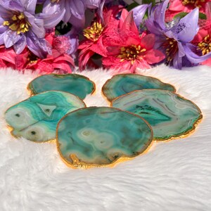 May include: Set of four green agate coasters with gold trim. The coasters are irregularly shaped and have a natural, organic look.