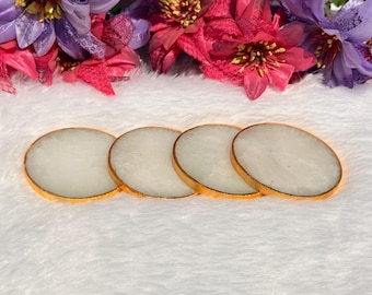 May include: Set of four white agate coasters with gold trim. The coasters are round and have a smooth, polished surface.