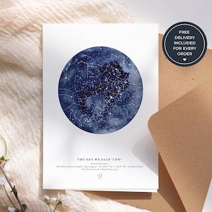 May include: A wedding card featuring a dark blue watercolour depiction of a starry night sky. The text "THE DAY WE SAID 'I DO'" is printed below the image, along with names, a location, and a date. A brown envelope is partially visible.