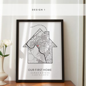 May include: A black framed print with a gray and white map of a city in the shape of a house. The text "Our First Home" is below the map, along with the names "Sarah & Steve" and the coordinates "51.4545" N, 2.5879" W.