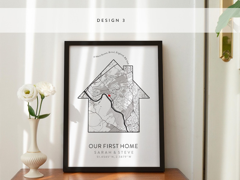 Op de afbeelding: Een zwart ingelijst afdruk met een witte achtergrond met een kaart van een wijk in de vorm van een huis. De tekst "OUR FIRST HOME" is onder de kaart gedrukt, samen met de namen "SARAH & STEVE" en de co&ouml;rdinaten "51.4545" N, 2.5879" W.