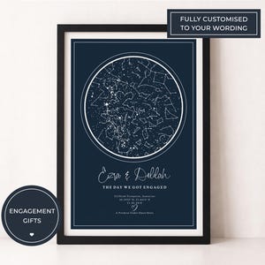 Puede incluir: Impresión enmarcada en azul marino con un mapa estelar blanco en un círculo. El texto "Ezra & Delilah" y "THE DAY WE GOT ENGAGED" están debajo. La impresión está en un marco negro. Una pegatina circular dice "ENGAGEMENT GIFTS".