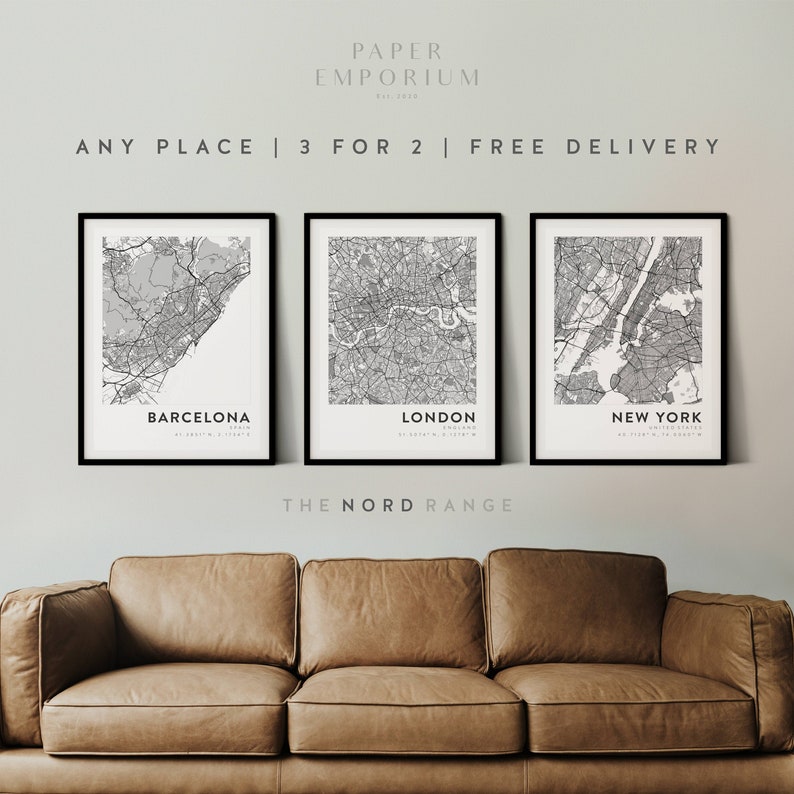 May include: Three black framed prints of city maps with the city names Barcelona, London, and New York printed below each map. The text "PAPER EMPORIUM" is at the top of the image and the text "ANY PLACE | 3 FOR 2 | FREE DELIVERY" is below it. The text "THE NORD RANGE" is below the prints.