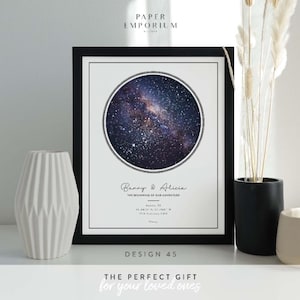 May include: Framed print featuring a circular image of a starry galaxy. The print includes the names "Banny & Alicia" and the text "THE BEGINNING OF OUR ADVENTURE." The frame is black, and the print is displayed with a white vase and decorative plants.
