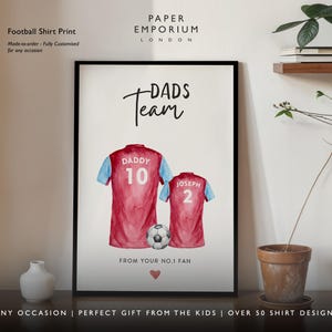 Op de afbeelding: Een printbaar ontwerp voor een voetbalshirt met twee aquarel shirts met de tekst "Dads Team" en "From your No.1 Fan". De shirts zijn rood en blauw met de nummers 10 en 2.