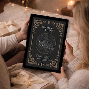 May include: A framed black print with gold detailing, displaying the text "THE DAY WE SAID 'I DO'". The print shows a star map within a circle, with names and a date. The frame is held by a person.