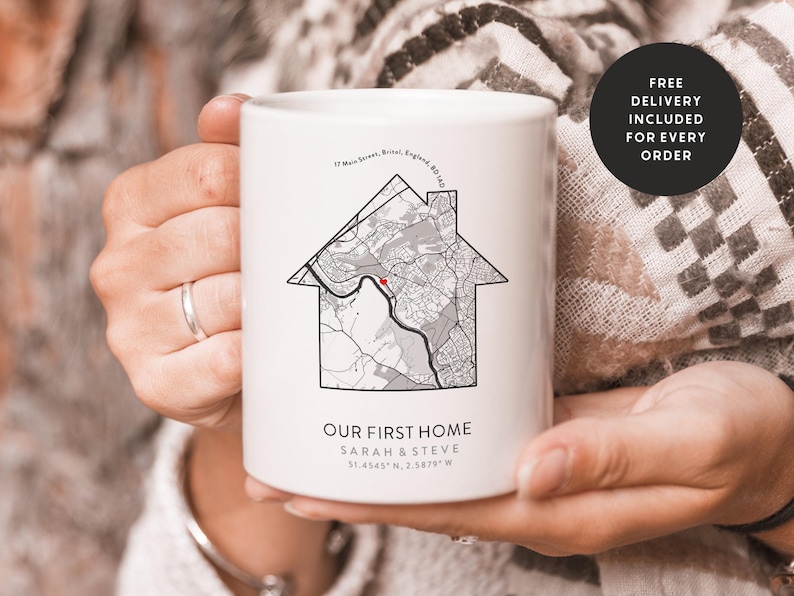 Op de afbeelding: Een witte keramische mok met een zwart-witte kaartontwerp van een wijk. De mok heeft de tekst "Onze eerste woning" en de namen "Sarah & Steve" met co&ouml;rdinaten.