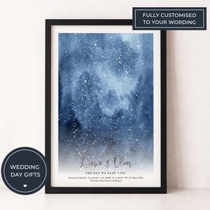 Peut inclure: Une impression encadrée avec un fond bleu foncé à l'aquarelle ressemblant à un ciel étoilé. L'impression comprend les noms "Darcie & Oliver" et le texte "THE DAY WE SAID I DO". Le cadre est noir et l'impression est étiquetée "WEDDING DAY GIFTS".
