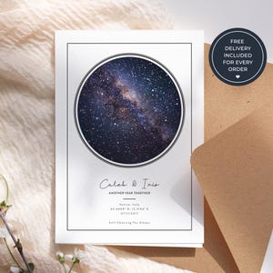 以下が含まれることがあります： 星空の円形画像が中央に配置された白い長方形のプリント。黒い枠線の中に「Caleb & Iris」「ANOTHER YEAR TOGETHER」「Venice, Italy」「45.4408 N, 12.3155 E」「07/11/2017」「Still Choosing You Always」というテキストが記載されています。