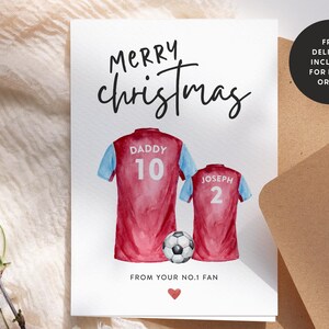 Op de afbeelding: Een kerstkaart met een aquarel-illustratie van twee voetbalshirts met de namen "Daddy" en "Joseph" en de nummers "10" en "2" erop. De kaart zegt "Merry Christmas" en "Van je No.1 Fan".