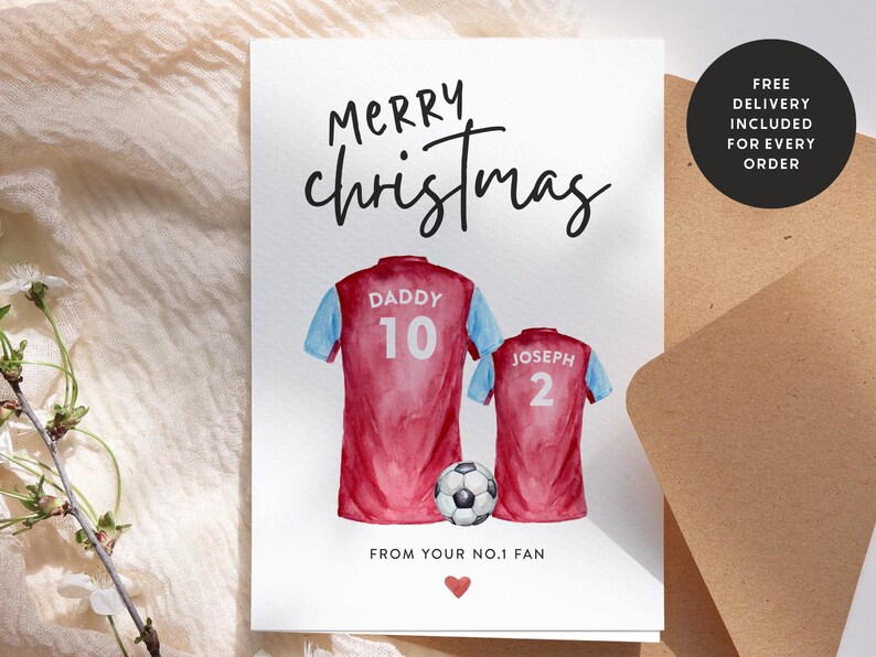 Op de afbeelding: Een kerstkaart met een aquarel-illustratie van twee voetbalshirts met de namen "Daddy" en "Joseph" en de nummers "10" en "2" erop. De kaart zegt "Merry Christmas" en "Van je No.1 Fan".