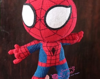 May include: A handmade crochet Spider-Man doll. The doll features a red head and hands with a black web pattern, white eyes, and a blue and red body. The doll is posed with arms outstretched.