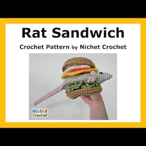 May include: A crocheted rat shaped like a sandwich. The rat is gray and has a brown bun, yellow cheese, green lettuce, and a red tomato. The rat is holding a sandwich in its paws. The text "Rat Sandwich" and "Crochet Pattern by Nichet Crochet" is displayed above the image.