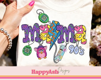 May include: White t-shirt with a colorful "Mama 90's" graphic. The design includes a lightning bolt, a Furby, a retro phone, and a Tamagotchi. The shirt is held up by a person.