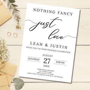 Könnte beinhalten: Eine weiße Hochzeitseinladung mit schwarzer Schrift, die „Nothing Fancy, Just Love“ lautet. Die Einladung enthält die Namen Leah & Justin, das Datum 27. August 20XX und die Uhrzeit 18:00 Uhr. Goldene Eheringe und Schreibwaren sind im Hintergrund.