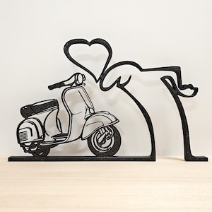 Può includere: Scultura in metallo nero di uno scooter vintage con un design a forma di cuore sopra. Lo scooter è dettagliato con un sedile, manubrio e ruote. La scultura è su una base rettangolare.