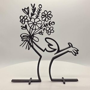 Könnte beinhalten: Schwarze Metallsculptur einer Person, die einen Blumenstrauß hält. Die Skulptur steht auf einem schwarzen Metallsockel mit drei Beinen.