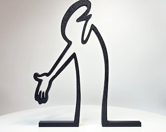 May include: A black, flat, two-dimensional sculpture depicting a stylized human-like figure with a curved head and torso, featuring one extended arm with a hand reaching downward, supported by two horizontal base bars on a plain white surface.