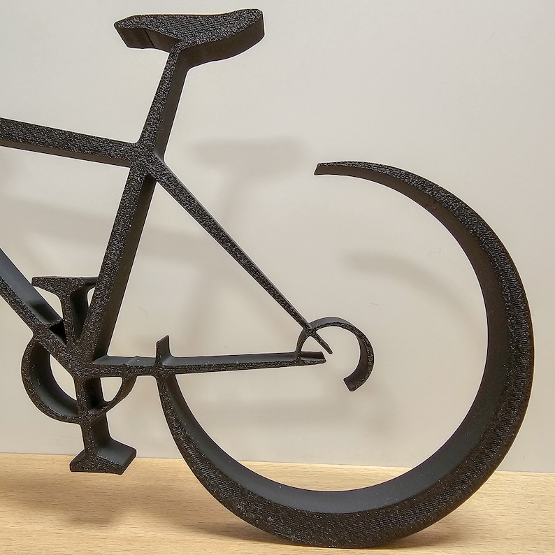 Puede incluir: Escultura de bicicleta de metal negro con un marco curvo y una sola rueda. La escultura est&aacute; hecha de metal delgado y tiene un dise&ntilde;o minimalista.