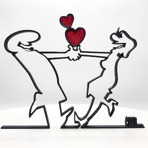 Peut inclure: Sculpture stylisée noire représentant deux personnages tenant deux cœurs rouges. Les personnages sont reliés par une ligne horizontale, avec le mot "CAVA" à la base. L'œuvre est une représentation moderne de l'amour et des relations.