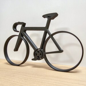 May include: Black metal silhouette of a bicycle with a curved frame and thin wheels.