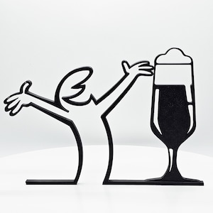 Op de afbeelding: Zwarte silhouet van een persoon die zijn armen in de lucht steekt in een viering, met een glas bier met een schuimkraag. Het silhouet is uit hout gesneden en staat op een voet.