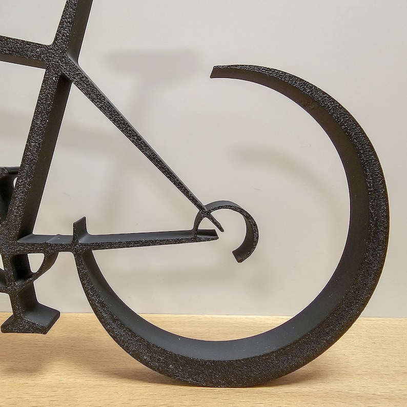 Puede incluir: Escultura de metal negro de una bicicleta con una sola rueda. La escultura est&aacute; hecha de metal delgado y tiene un dise&ntilde;o minimalista.