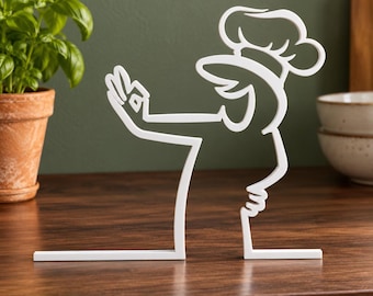 May include: A white, flat, linear metal sculpture depicting a chef wearing a tall toque hat. The figure is shown in profile, with one arm extended forward and the hand forming an okay gesture. The design is composed of a single continuous line.