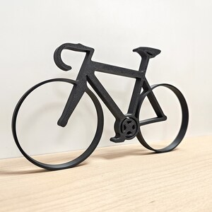 May include: Black metal silhouette of a bicycle with two wheels. The bicycle is a road bike with a curved handlebar and a thin frame.