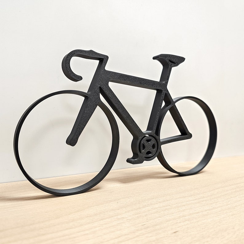 May include: Black metal silhouette of a bicycle with two wheels. The bicycle is a road bike with a curved handlebar and a thin frame.