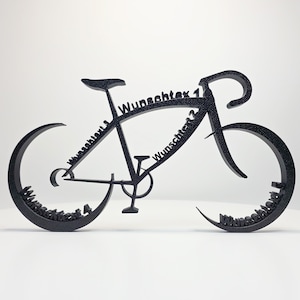 Op de afbeelding: Zwarte metalen fietssculptuur met het woord "Wunschtext" in script. De sculptuur is een gestileerde weergave van een racefiets, met gebogen wielen en stuur. De tekst wordt op verschillende plaatsen op de fiets herhaald.