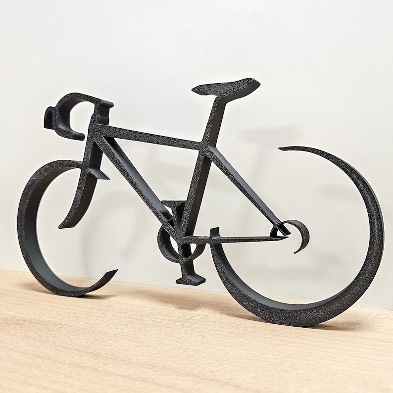 Puede incluir: Silueta negra de metal de una bicicleta con un cuadro curvo y ruedas finas. La bicicleta es una pieza de arte de pared decorativa.