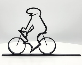 May include: Black silhouette of a person riding a bicycle. The cyclist is depicted with a simple, stylized design, with a rounded head and body. The bicycle has two wheels and is mounted on a rectangular base.
