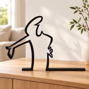 Può includere: Una scultura in metallo nero caratterizzata da un design a linea continua che forma la sagoma di una figura che tende un braccio. L'oggetto presenta una base piatta ed è realizzato in un unico pezzo di metallo scuro con finitura opaca.