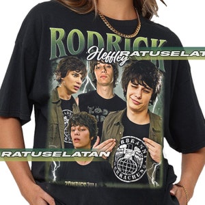 Pode incluir: Camiseta preta com uma estampa gráfica de Rodrick Heffley da série de livros "Diário de um Banana". O gráfico apresenta Rodrick em diferentes poses com o texto "Rodrick Heffley" e "Zombies Will" impresso na camiseta.