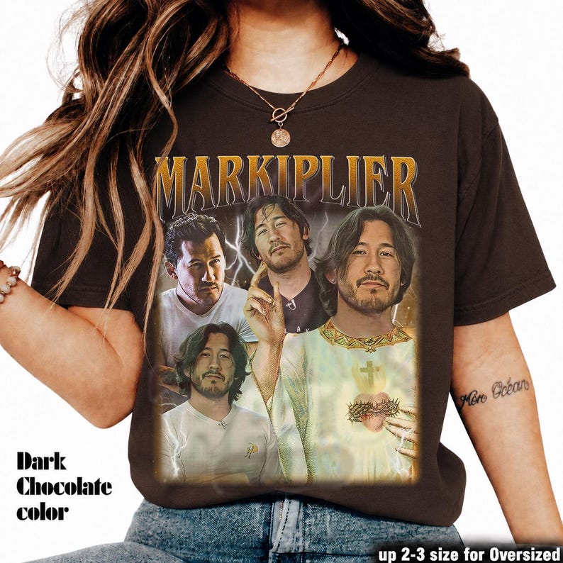 May include: Dark chocolate-colored t-shirt featuring a vintage-style graphic of Markiplier. The design includes multiple images of Markiplier with the name "MARKIPLIER" in gold lettering. The text "up 2-3 size for Oversized" is also visible.