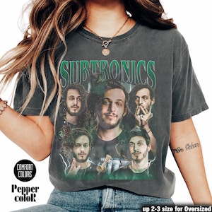 May include: Dark gray Comfort Colors t-shirt with a green and white graphic of the word "SUBTRONICS" above a collage of five men. The shirt also features the text "Pepper color" and "up 2-3 size for Oversized".